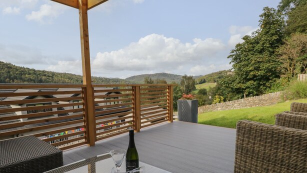 An outdoor deck with wicker furniture, a glass table, and a bottle of wine. - Bishop Fell (Ulverston)