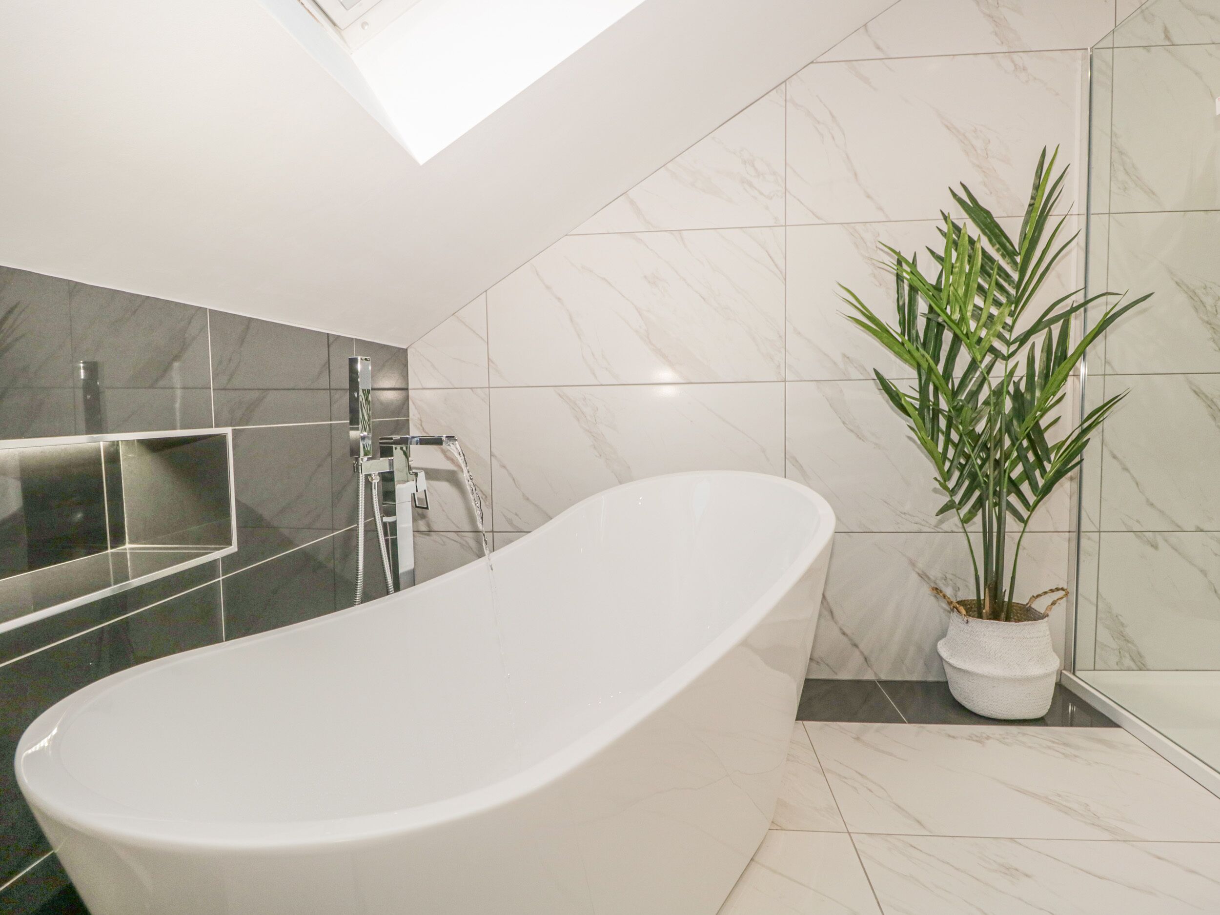 Un baño moderno con una bañera independiente, ducha y una planta en maceta.
