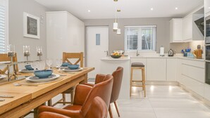 A modern kitchen with white cabinets, a wooden dining table, and brown leather chairs. - Bishop Fell (Ulverston)