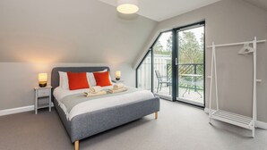 Et moderne soveværelse med en stor seng, to sengeborde med lamper, et vindue med udsigt over naturen og en loftlampe.
