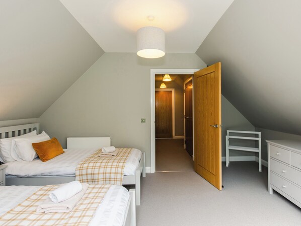 A bedroom with a sloped ceiling, two beds, a wooden wardrobe, and a desk.