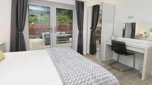Ein modernes Schlafzimmer mit einem Bett, einem Schreibtisch und einer großen Schiebeglasdoor, die auf eine Terrasse im Freien führt.