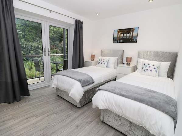 A double room with two beds, a balcony with a table and chairs, and a painting on the wall.