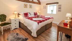 A bedroom with a wooden ceiling, a bed with red and white bedding, a green chair, a nightstand, and a window with a plant. - Cut Moch, Plas Moelfre Hall Barns (Oswestry)