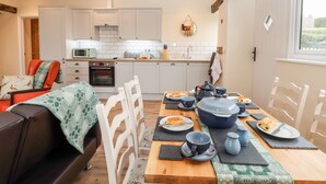A cozy kitchen with wooden beams, white cabinets, and a dining table set with plates, cups, and a large pot. - Cut Moch, Plas Moelfre Hall Barns (Oswestry)