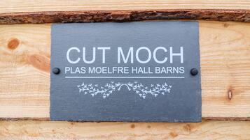 Un letrero de pizarra con la inscripción 'CUT MOCH' y 'PLAS MOELFRE HALL BARNS', sujeto a una pared de madera.