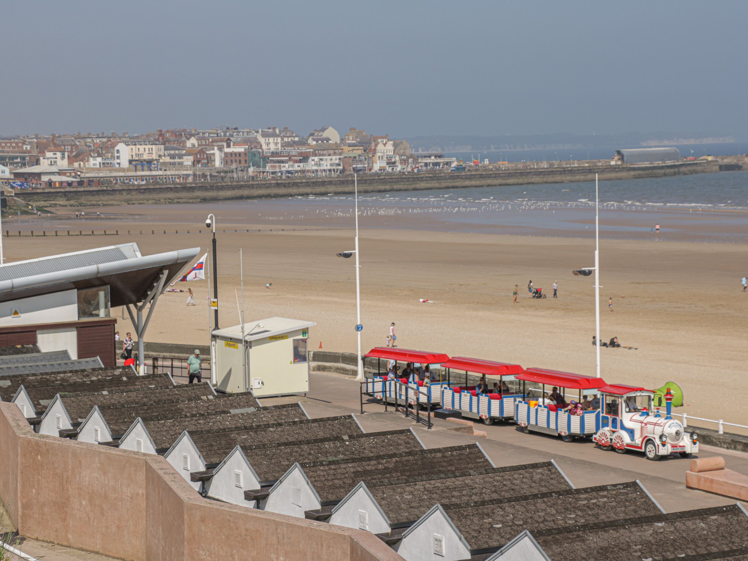 A seaside train ride with a coastal view, a beach, and a row of houses in the background.