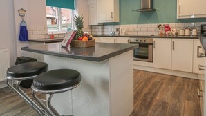 A modern kitchen with white cabinets, a stainless steel oven, and a fruit basket on the counter. - Cosy Coast Cottage (Bridlington)