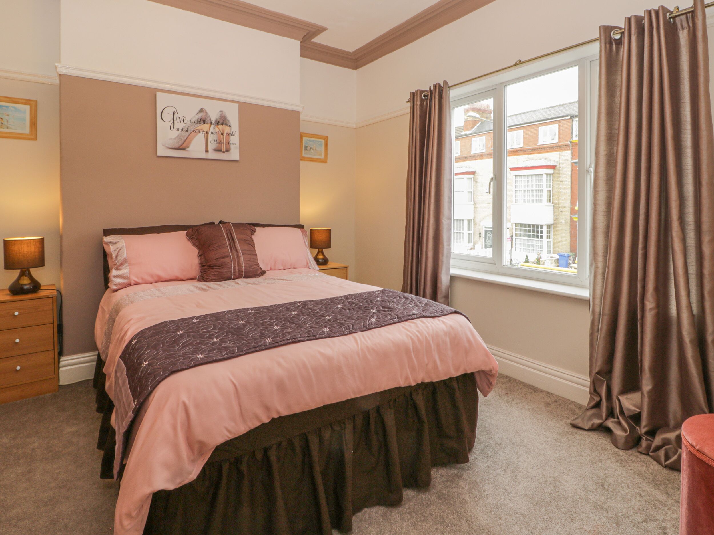 A bedroom with a bed, two bedside tables, a window with curtains, and a wall with a framed picture.