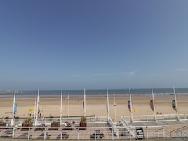 Vista de la playa con un paseo marítimo, banderas y un letrero que indica un café/bar.