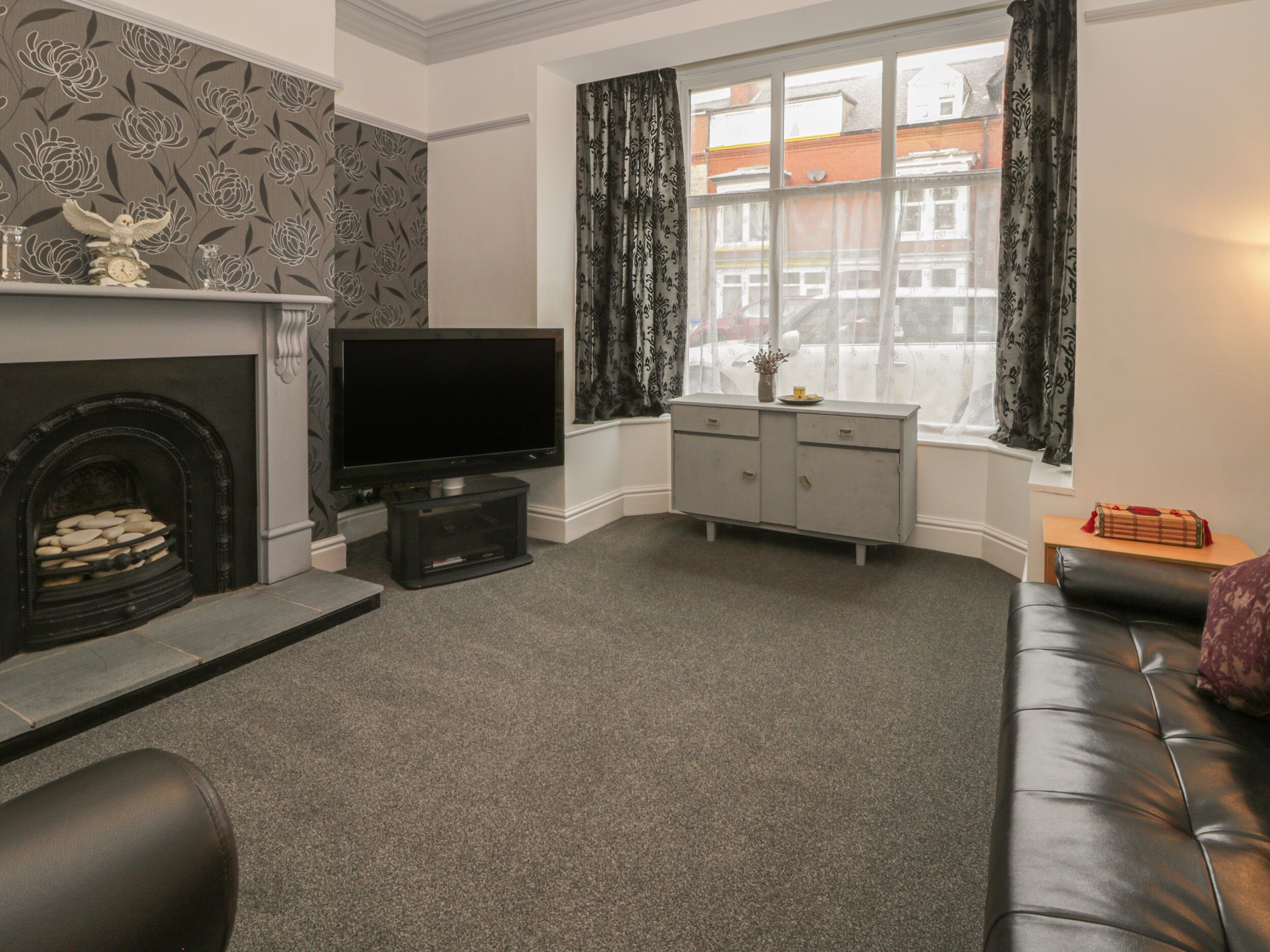 A living room with a fireplace, a flat-screen TV, a grey cabinet, and a black leather sofa.