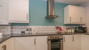 A modern kitchen with white cabinets, a stainless steel range hood, a built-in oven, and a microwave. - Cosy Coast Cottage (Bridlington)