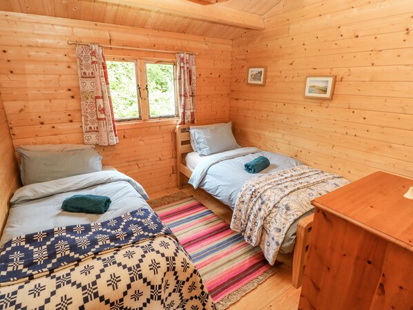 A wooden cabin room with two beds, a wooden desk, and a window with curtains. - The Beach Shack (Carmarthen)