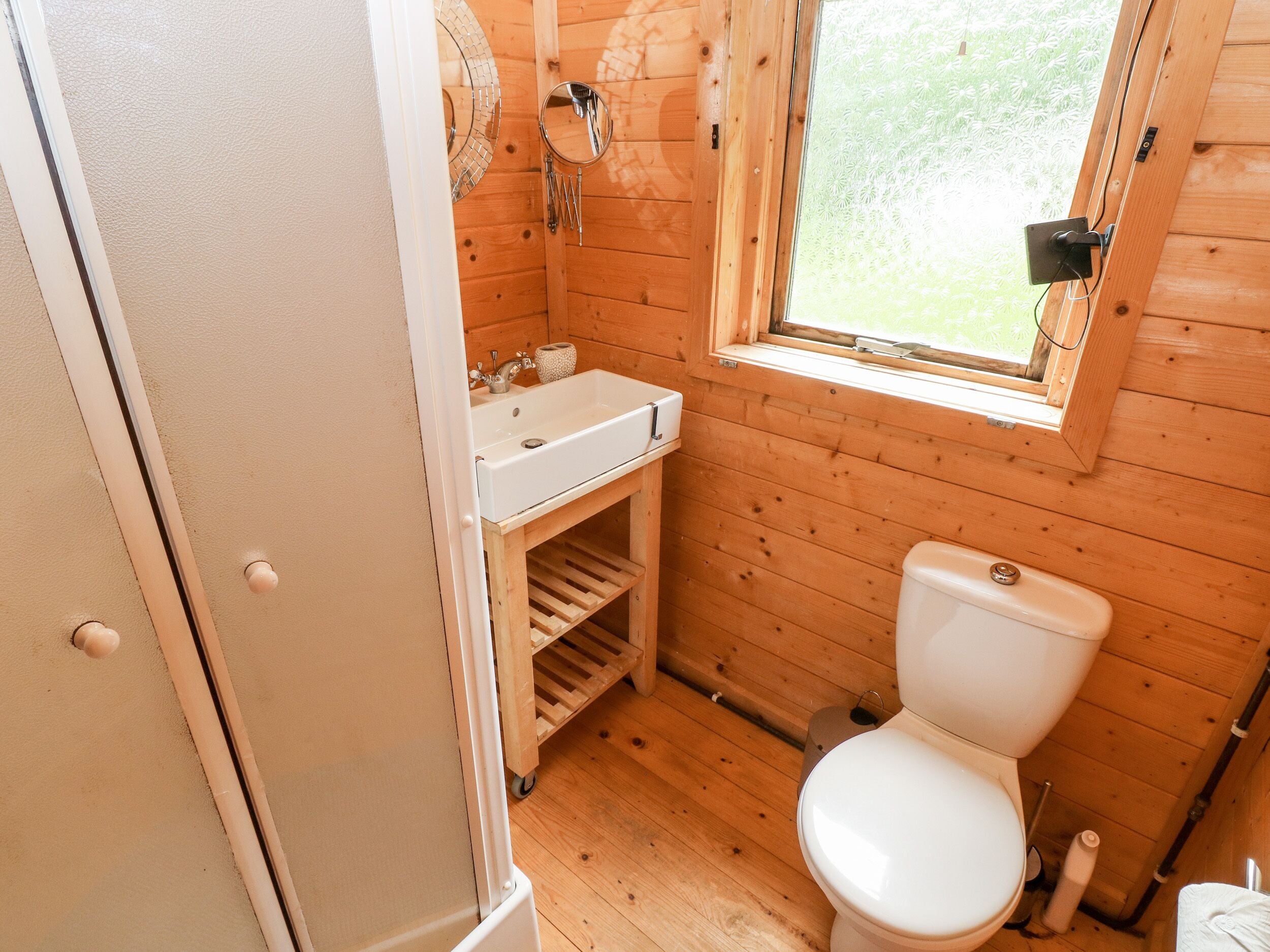 A compact wooden bathroom with a white sink, a toilet, and a window.