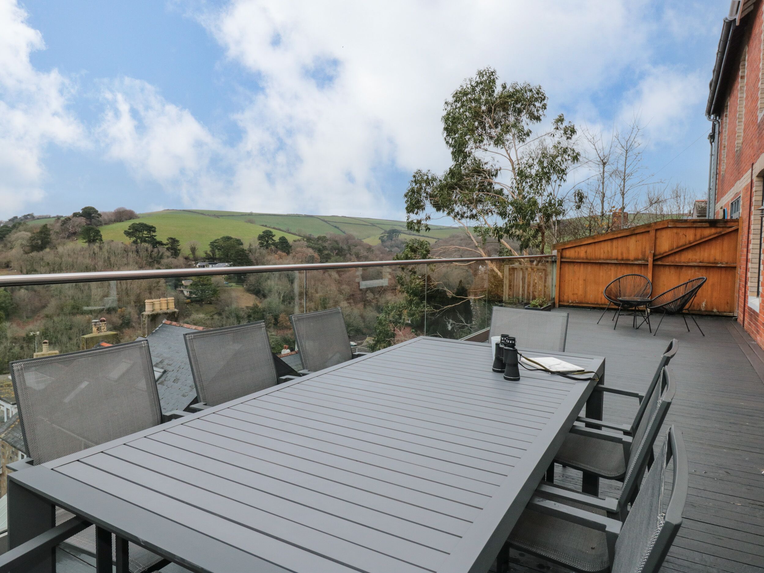 A deck with a table and chairs, overlooking a hilly landscape.