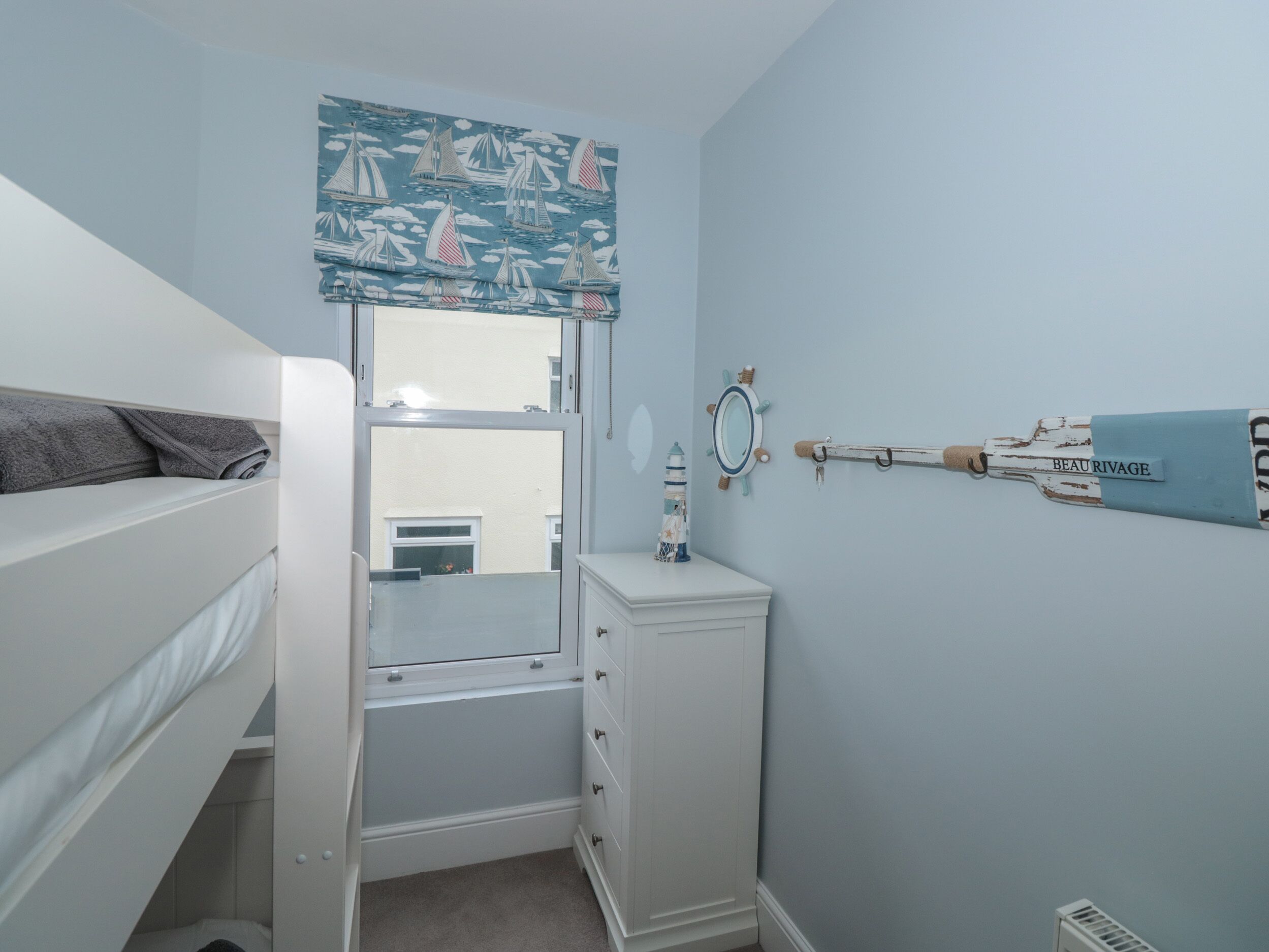 Ein Schlafzimmer mit Etagenbett, Kommode, Spiegel und einem an der Wand befestigten Regal mit einer Flasche mit dem Aufdruck 'BEAU RIVAGE'.