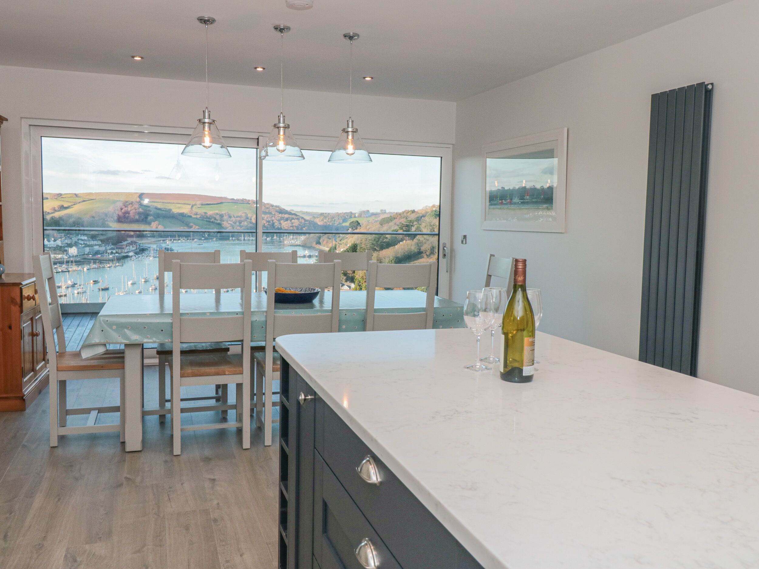 A modern kitchen with a large island, white cabinetry, and a view of a harbor.