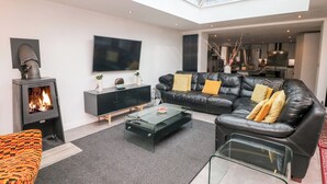 A modern living room with a fireplace, a black leather sofa, a glass coffee table, and a flat-screen TV. - Carr House Farm (Glossop)
