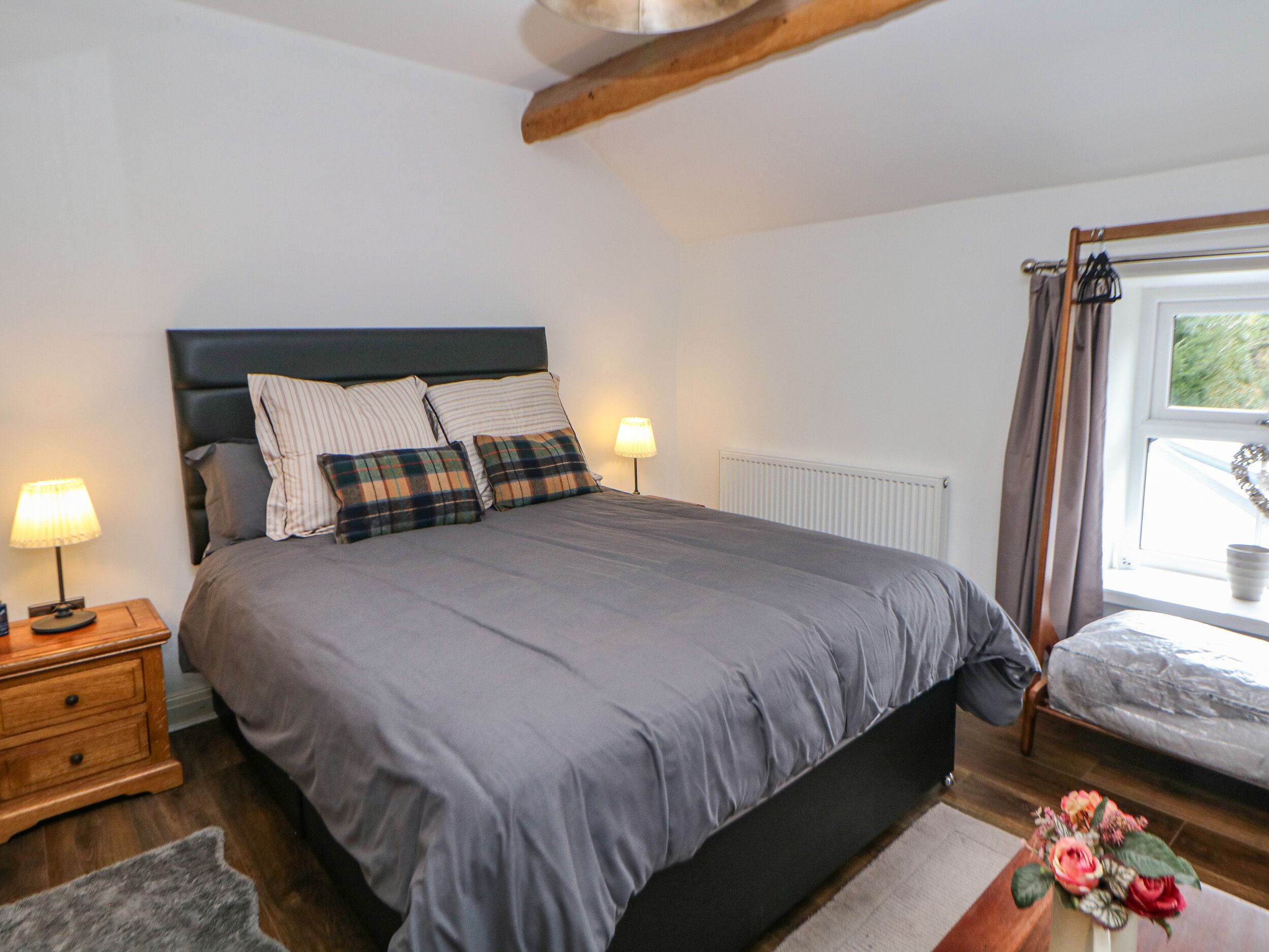A bedroom with a bed, nightstands, a window with curtains, and a small table with a vase.