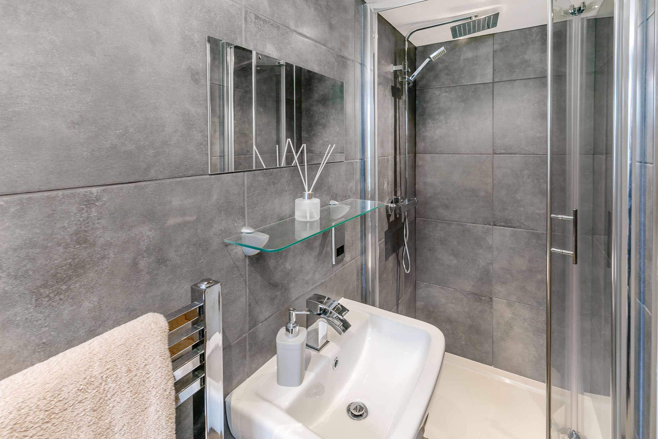 Un bagno moderno con cabina doccia in vetro, un lavabo bianco con accessori cromati e uno scaffale in vetro sopra il lavabo.