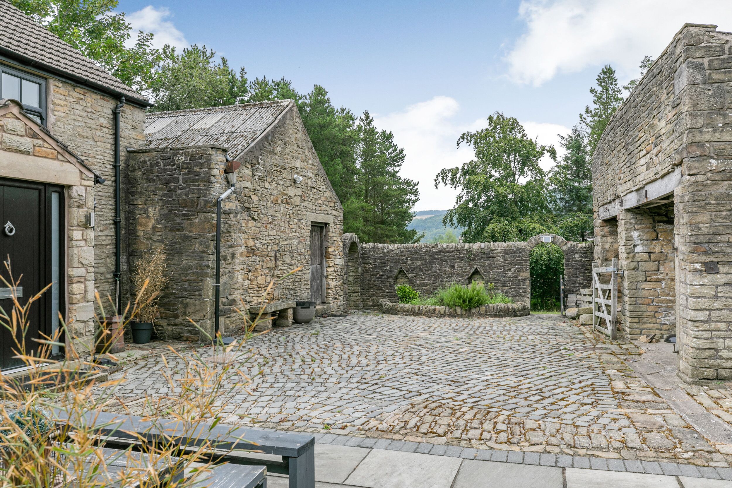 A stone building with a cobblestone courtyard, a wooden door, and a view of the surrounding landscape.