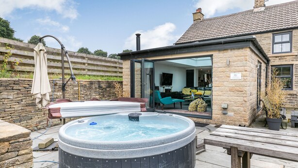 A hot tub in a backyard with a stone house, a wooden deck, and a patio table. - Carr House Farm (Glossop)