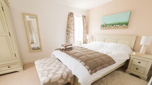 Un dormitorio con una cama, una mesita de noche, un banco, un aparador, un espejo y un cuadro en la pared.