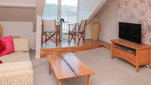 Una sala de estar acogedora con un sofá, una mesa de centro de madera, un mueble para televisión y un balcón con vistas.