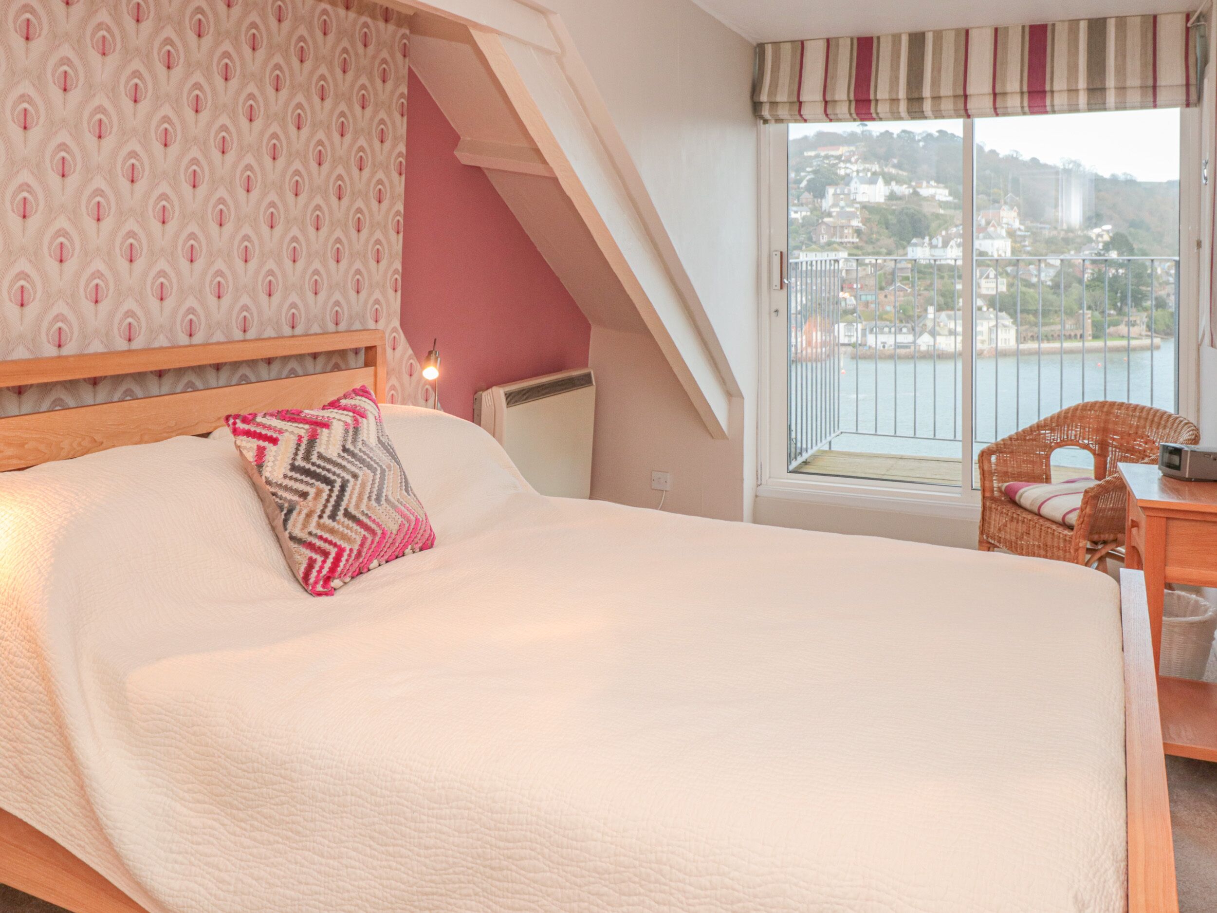 A bedroom with a large bed, a view of a balcony, and a wicker chair.