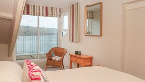 Un dormitorio con cama, una silla, una mesita, un espejo y ventana con vistas al mar.