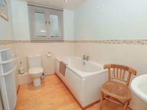 A bathroom with a toilet, bathtub, and wooden chair.