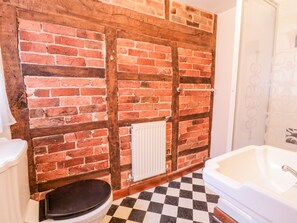 A bathroom with a brick wall, a white radiator, a black toilet, and a white bathtub.