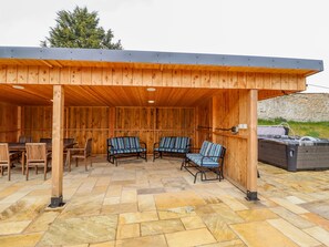 A covered outdoor seating area with stone flooring, wooden walls, and a stone wall in the background.