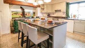 Una cocina con isla central, taburetes de bar, estufa y ventana con cortinas.