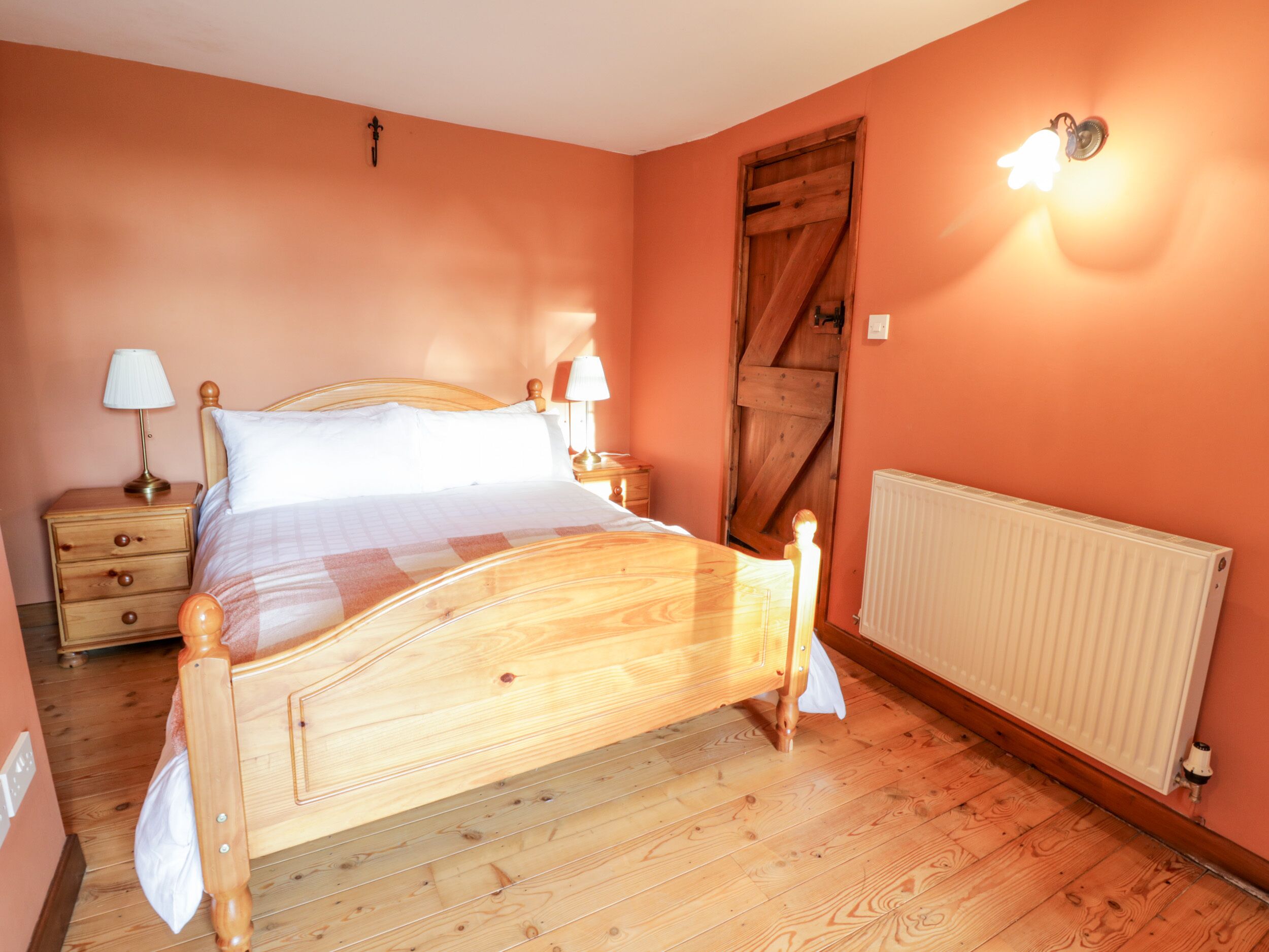A bedroom with a wooden bed, two bedside tables with lamps, a radiator, and a wooden door.