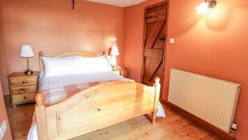 A bedroom with a wooden bed, two bedside tables with lamps, a radiator, and a wooden door.