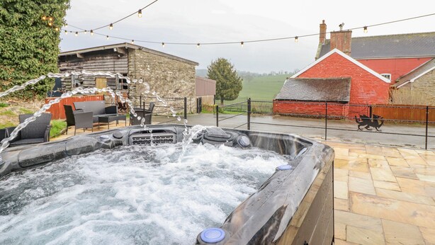 Un jacuzzi con chorros de agua, rodeado de asientos exteriores y un muro de piedra.