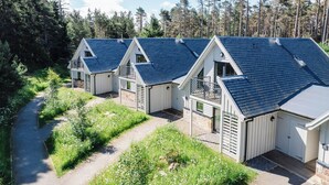 A row of cabins with sloped roofs, surrounded by a forested area and a dirt path. - Otter Lodge (Kingussie)