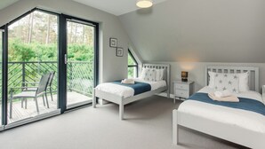 A bedroom with two beds, a balcony with a chair, and a view of greenery. - Otter Lodge (Kingussie)