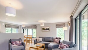 A modern living room with a grey sofa set, wooden coffee table, and a dining area with a table and chairs. - Otter Lodge (Kingussie)