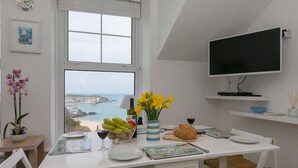 Un coin repas avec vue sur la mer, une horloge et un téléviseur accroché au mur.