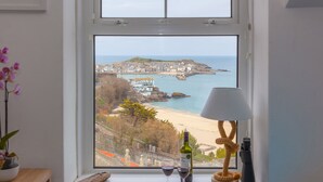 Une fenêtre donnant sur une ville côtière, une lampe et deux verres à vin posés sur le rebord de la fenêtre.