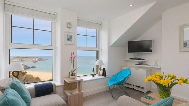 Un salon moderne avec vue sur la mer, comprenant un canapé, un fauteuil bleu et un téléviseur.