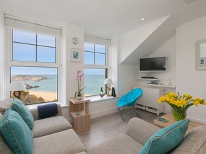 Uma sala de estar moderna com vista para o mar, um conjunto de sofá, uma poltrona azul e uma televisão.