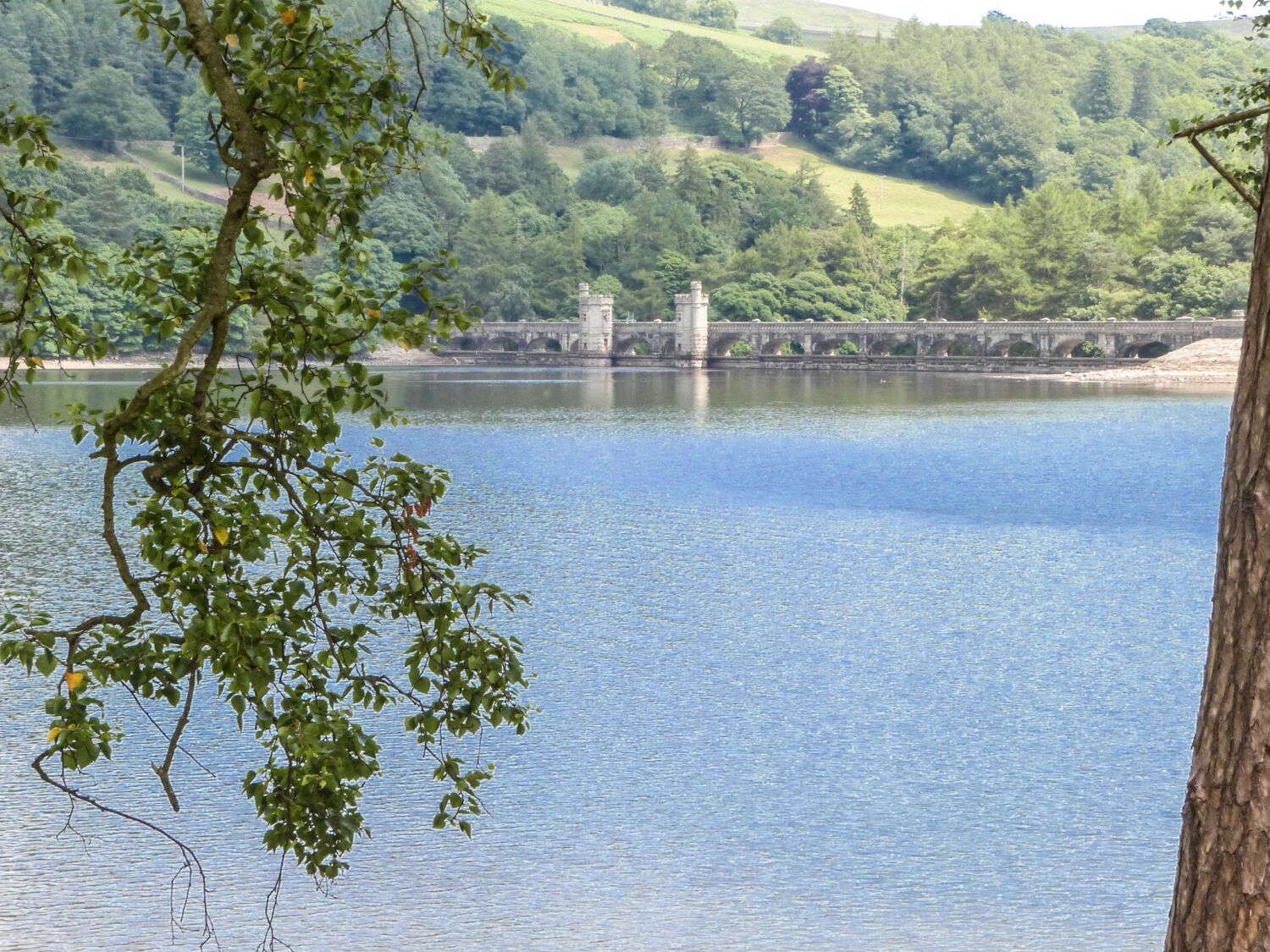 Ein ruhiger See mit einer Steinbrücke und einem Turm in der Ferne.