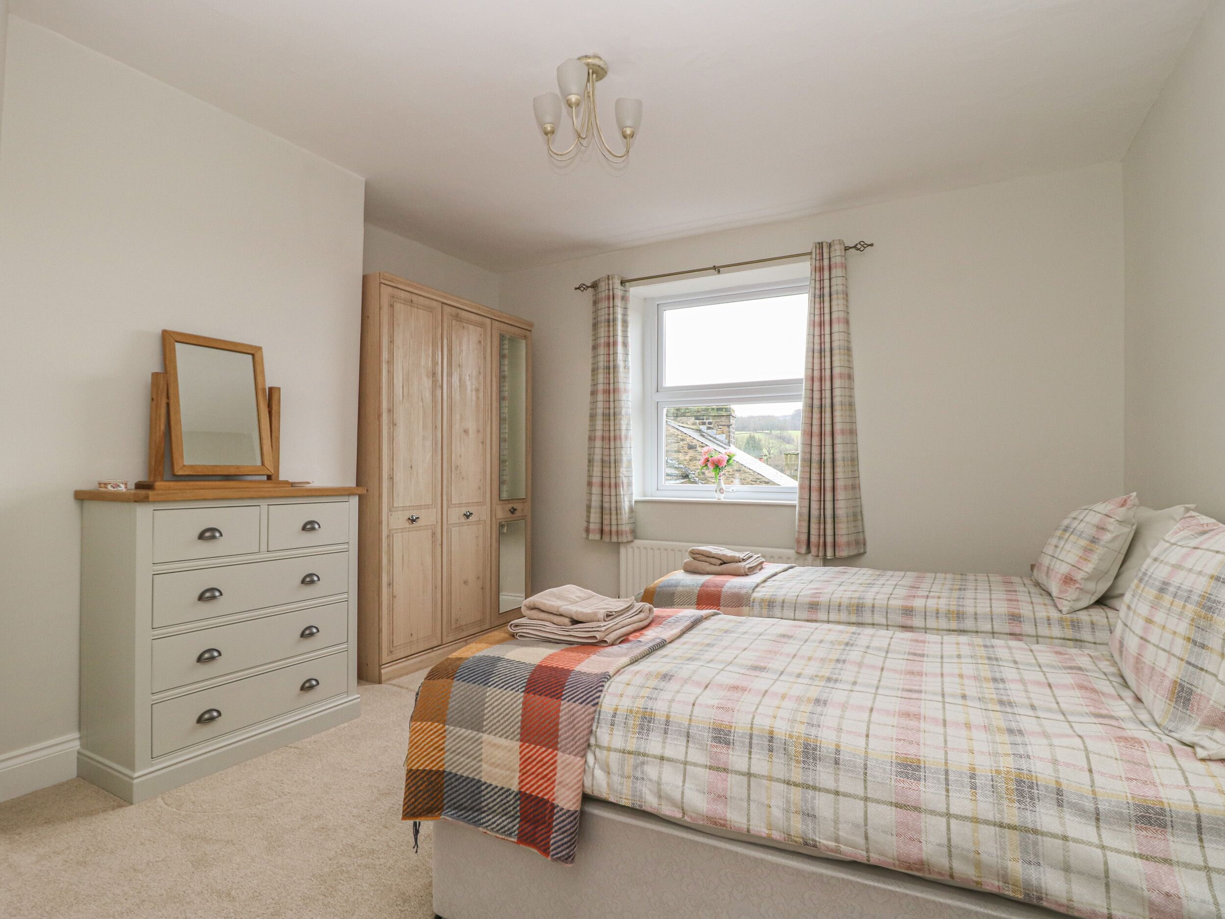 A bedroom with a bed, a dresser, a mirror, a window with curtains, and a view of a building outside.
