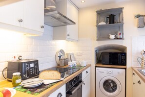 Une petite cuisine équipée d’un grille-pain, d’un four à micro-ondes, d’un lave-linge et d’une miche de pain posée sur le comptoir.