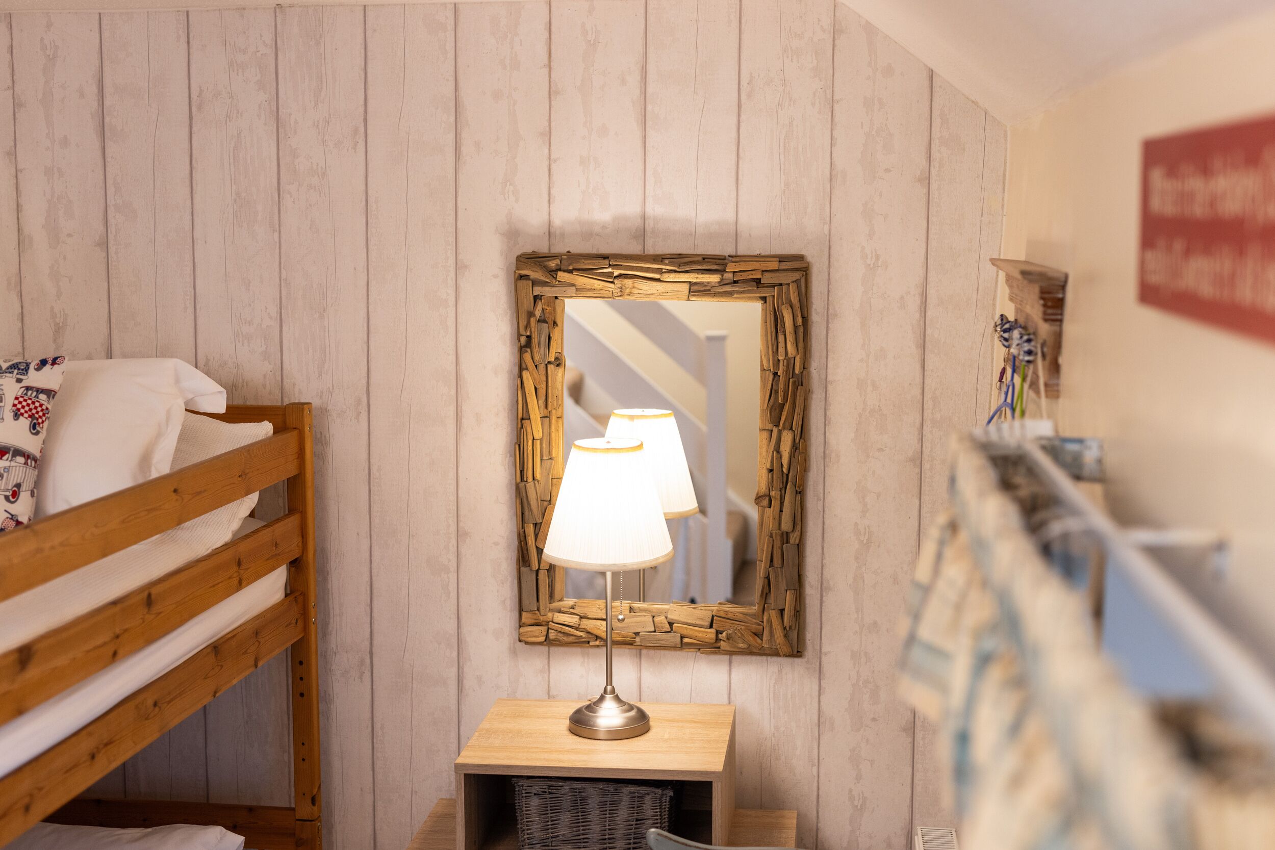 A room with a wooden bunk bed, a small table with a lamp, and a mirror with a wooden frame.