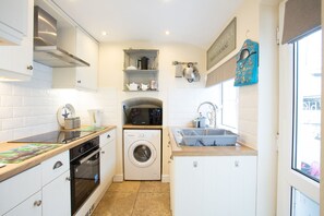A compact kitchen with a washing machine, a sink, and a microwave. - Old Post Office (Amlwch)