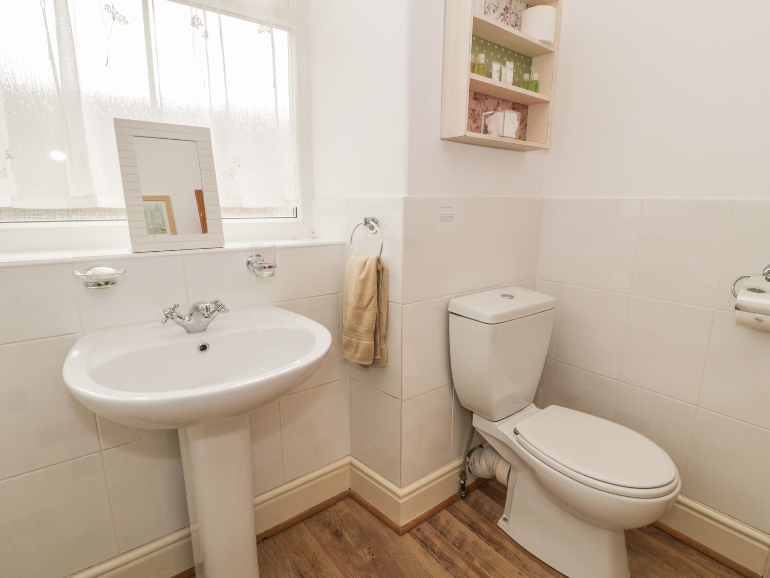 Een badkamer met een witte wastafel, toilet en houten vloer.
